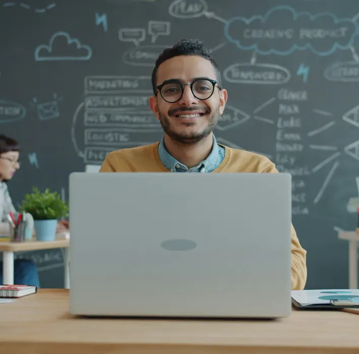 A smiling founder at his laptop in a startup office